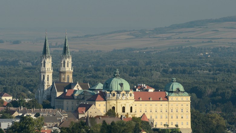 Stift Klosterneuburg, © Stift Klosterneuburg/Michael Zechany Luftaufnahme des Stifts Klosterneuburg mit zwei Türmen und einer Kuppel, umgeben von Wald und Feldern.