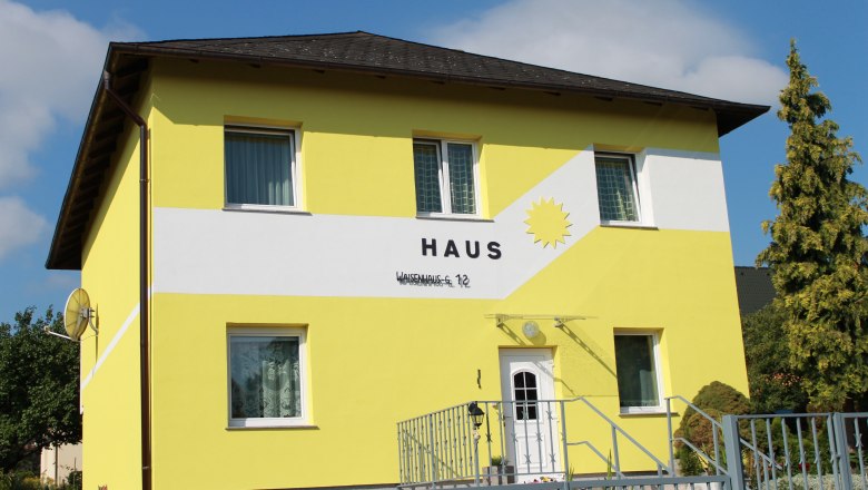 Yellow house with the inscription 'Haus' and a sun on the façade.