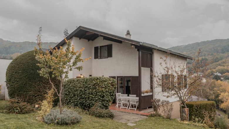 A two-storey house with garden and terrace, surrounded by trees and shrubs.