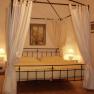 Ein Himmelbett mit weißen Vorhängen in einem gemütlichen Schlafzimmer, beleuchtet von zwei Nachttischlampen.
