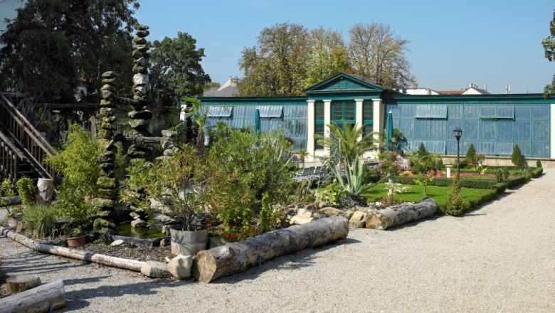 A well-tended garden with plants, a gravel path and a greenhouse in the background.