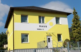 Yellow house with the inscription 'Haus' and a sun on the fa&ccedil;ade.
