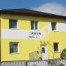 Gelbes Haus mit der Aufschrift 'Haus' und einer Sonne auf der Fassade.