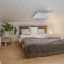 Cozy bedroom with sloping ceiling, bed, plants and lamp.