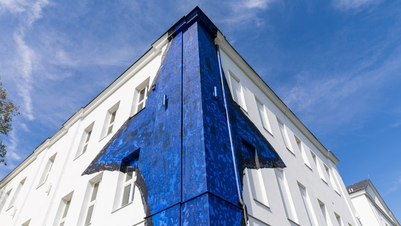 Geb&auml;ude mit blauer Wandkunst an der Ecke, vor blauem Himmel.