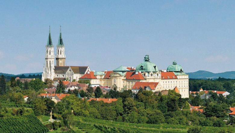 Panoramablick auf das Stift Klosterneuburg mit grünen Weinbergen im Vordergrund.