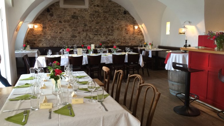 Gem&uuml;tlicher Gastraum mit gedeckten Tischen, Steinwand und gew&ouml;lbter Decke.
