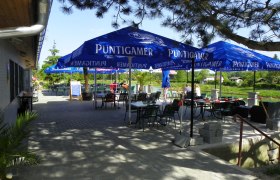 Au&szlig;enbereich eines Gasthauses mit blauen Sonnenschirmen und Tischen.