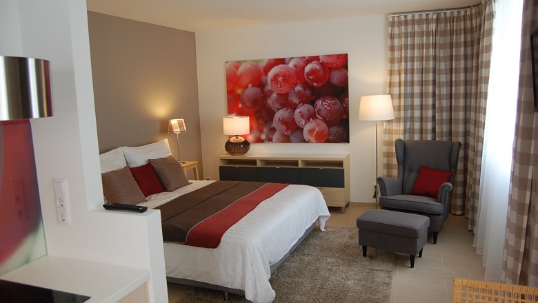 Modern eingerichtetes Schlafzimmer mit Doppelbett, Sessel und großem Bild von Weintrauben an der Wand.