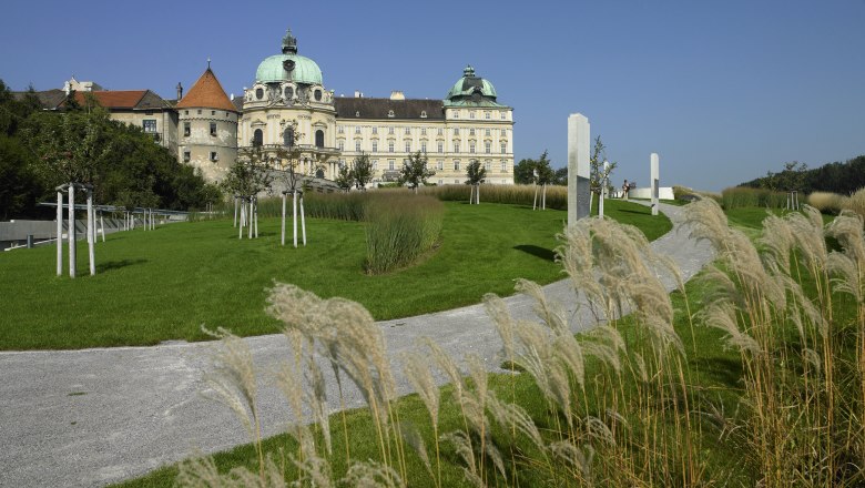 Castle with green roof, surrounded by well-kept garden and walkway.