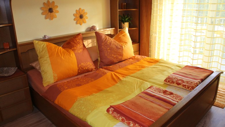 Gemütliches Schlafzimmer mit Sonnenblumen-Dekor und orange-gelber Bettwäsche.