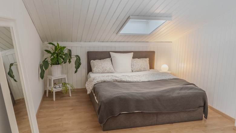 Gem&uuml;tliches Schlafzimmer mit Dachschr&auml;ge, Bett, Pflanzen und Lampe.