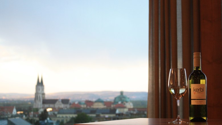 Weinflasche und Glas vor Stadtpanorama mit Kirche.