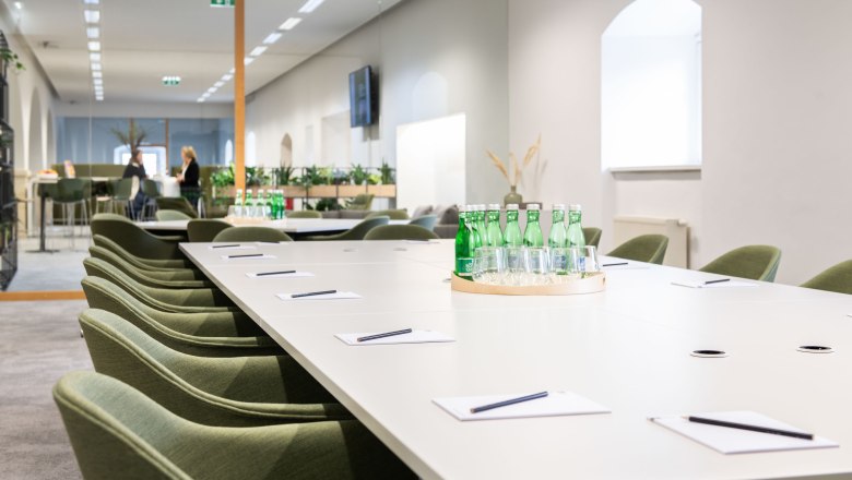 Modern conference room with long table, green chairs and water bottles.