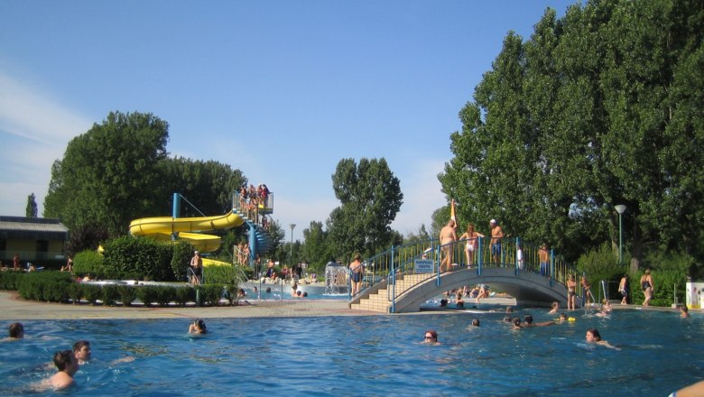 Outdoor pool with water slide and bridge, lots of people in the water.