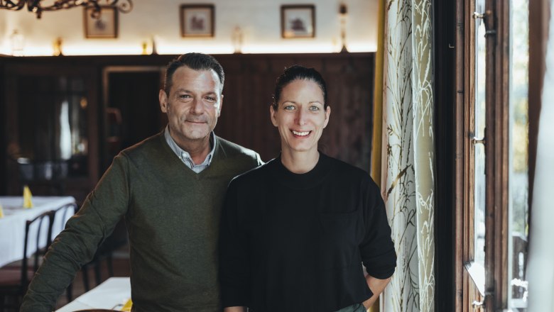 Ein Mann und eine Frau stehen l&auml;chelnd in einem gem&uuml;tlichen Restaurant.