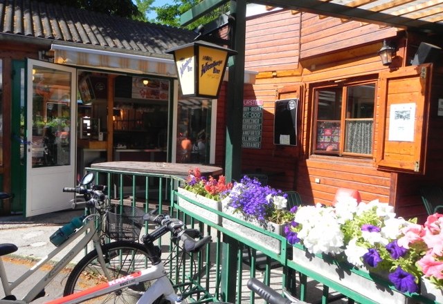 A cozy snack bar with wooden walls, bicycles and blooming flowers in the foreground.