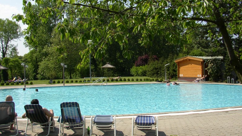 An outdoor pool in a park with sun loungers and trees in the background.