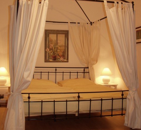 Himmelbett, © Hotel Residenz Schrannenhof Ein Himmelbett mit weißen Vorhängen in einem gemütlichen Schlafzimmer, beleuchtet von zwei Nachttischlampen.